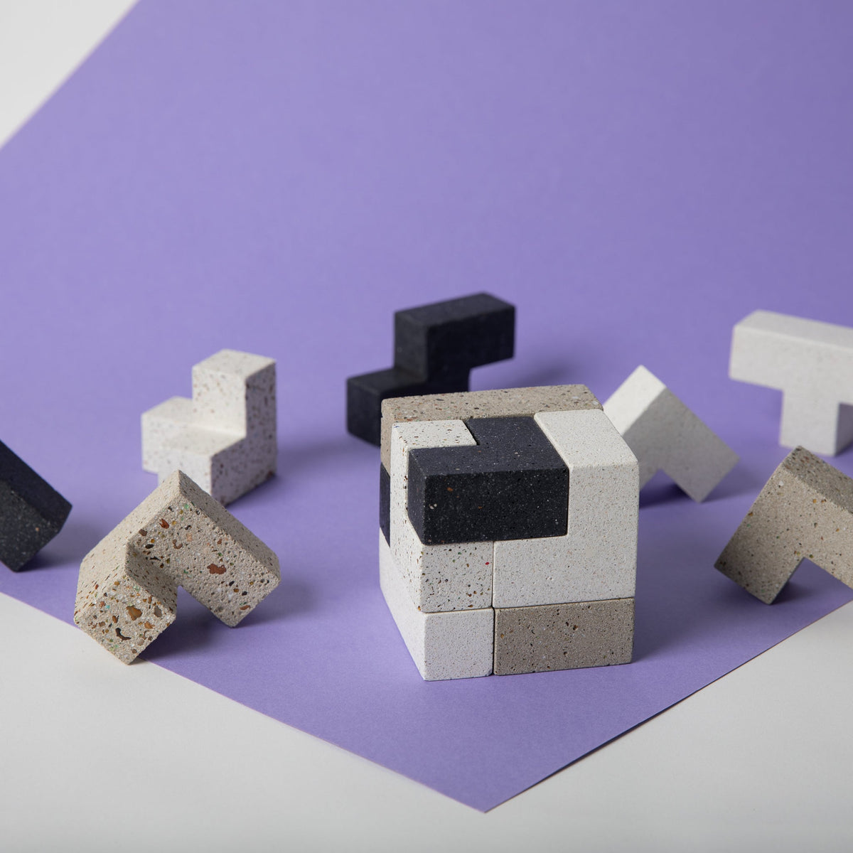 Brave New Cube terrazzo soma cube puzzle assembled on lilac paper, surrounded by its loose black, white and natural terrazzo pieces
