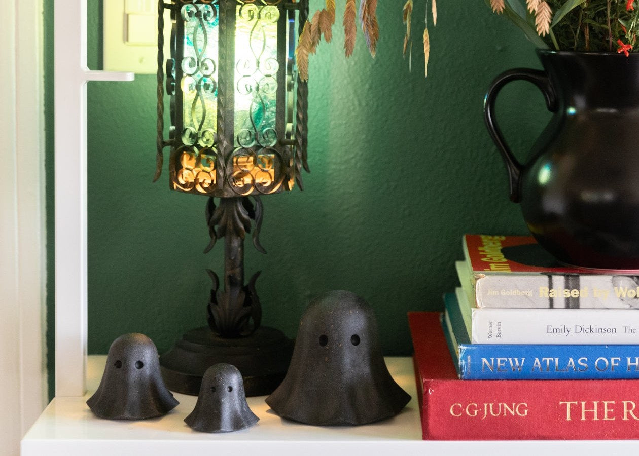 Black terrazzo concrete ghosts in three sizes on a bookshelf beside a glowing lantern lamp