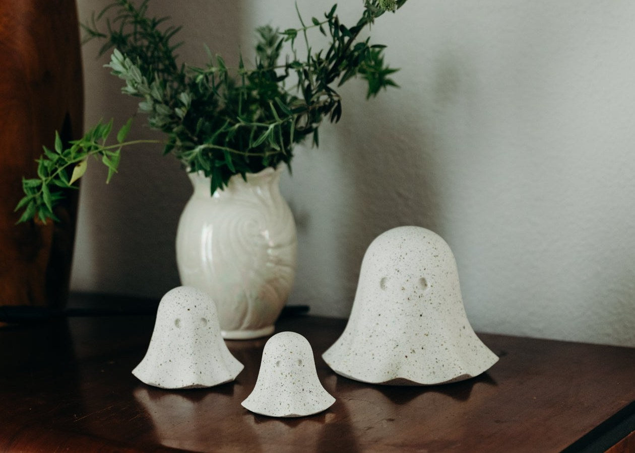 White terrazzo concrete ghosts in three sizes on a wooden dresser beside a vase of greenery